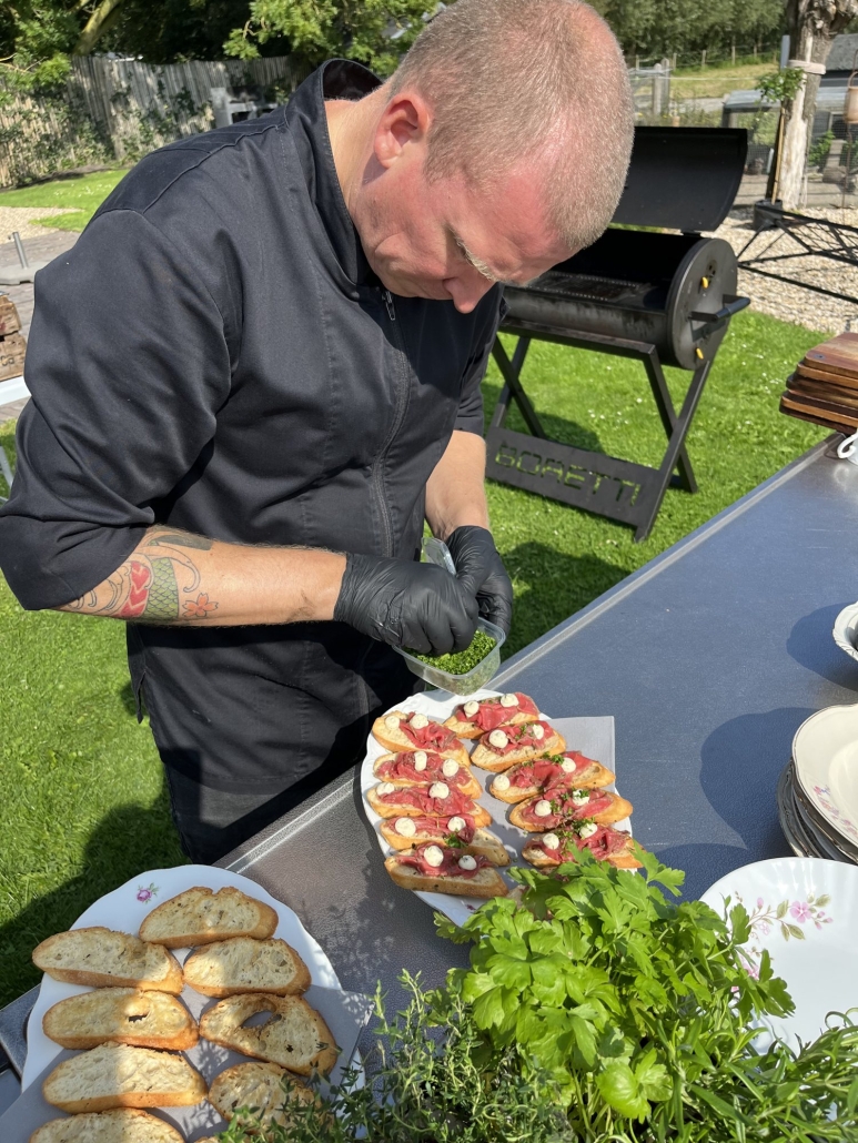 Kok van Offroad Catering grilt buiten op de BBQ tijdens een tuinfeest Kok van Offroad Catering grilt buiten op de BBQ tijdens een tuinfeest