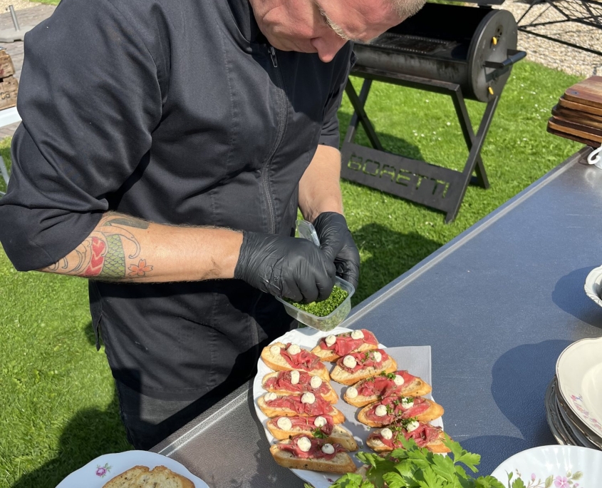 Kok van Offroad Catering grilt buiten op de BBQ tijdens een tuinfeest Kok van Offroad Catering grilt buiten op de BBQ tijdens een tuinfeest