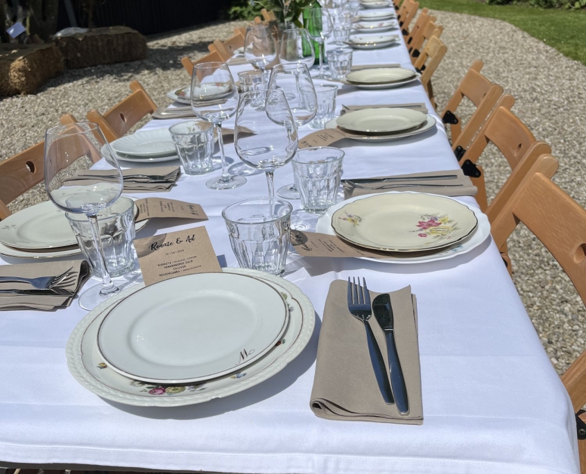Lange tafel met wit tafelkleed en brocante servies in een tuin Lange tafel met wit tafelkleed en brocante servies in een tuin, Offroad Catering