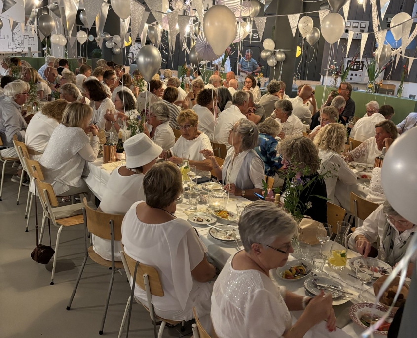 Gasten in het wit aan lange witte tafels tijdens een diner Gasten in het wit aan lange witte tafels tijdens een diner