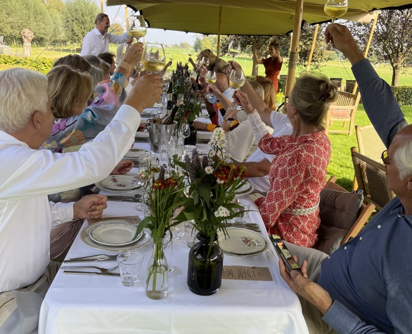 Gasten proosten aan een lange tafel onder een tent met uitzicht op de polder Gasten proosten aan een lange tafel onder een tent met uitzicht op de polder